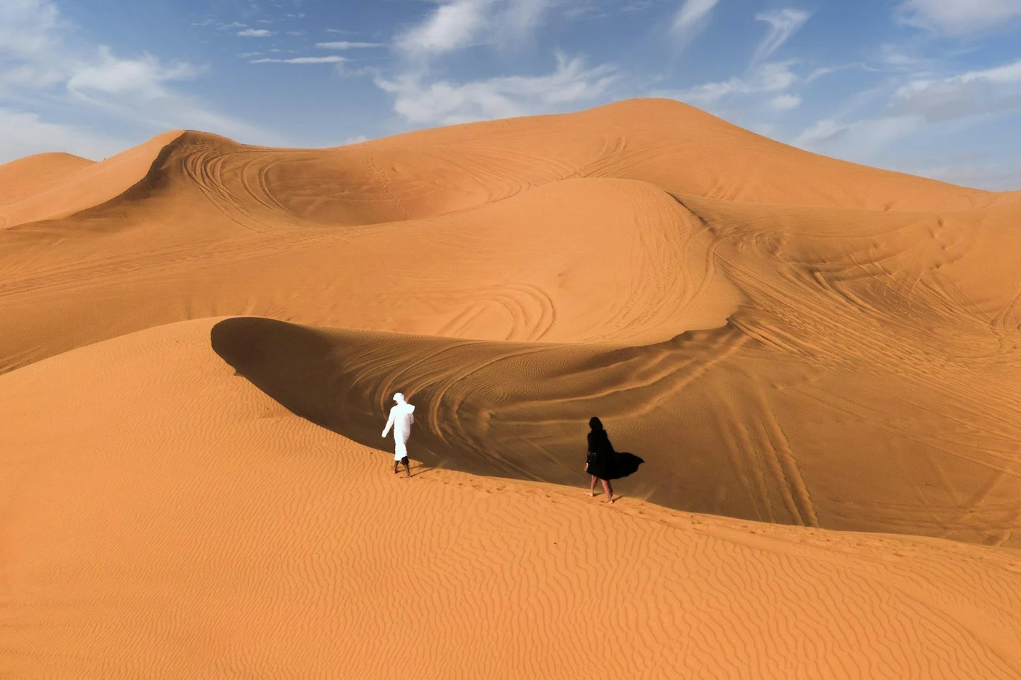 Zwei Personen in traditioneller Kleidung wandern durch die Sanddünen bei Dubai