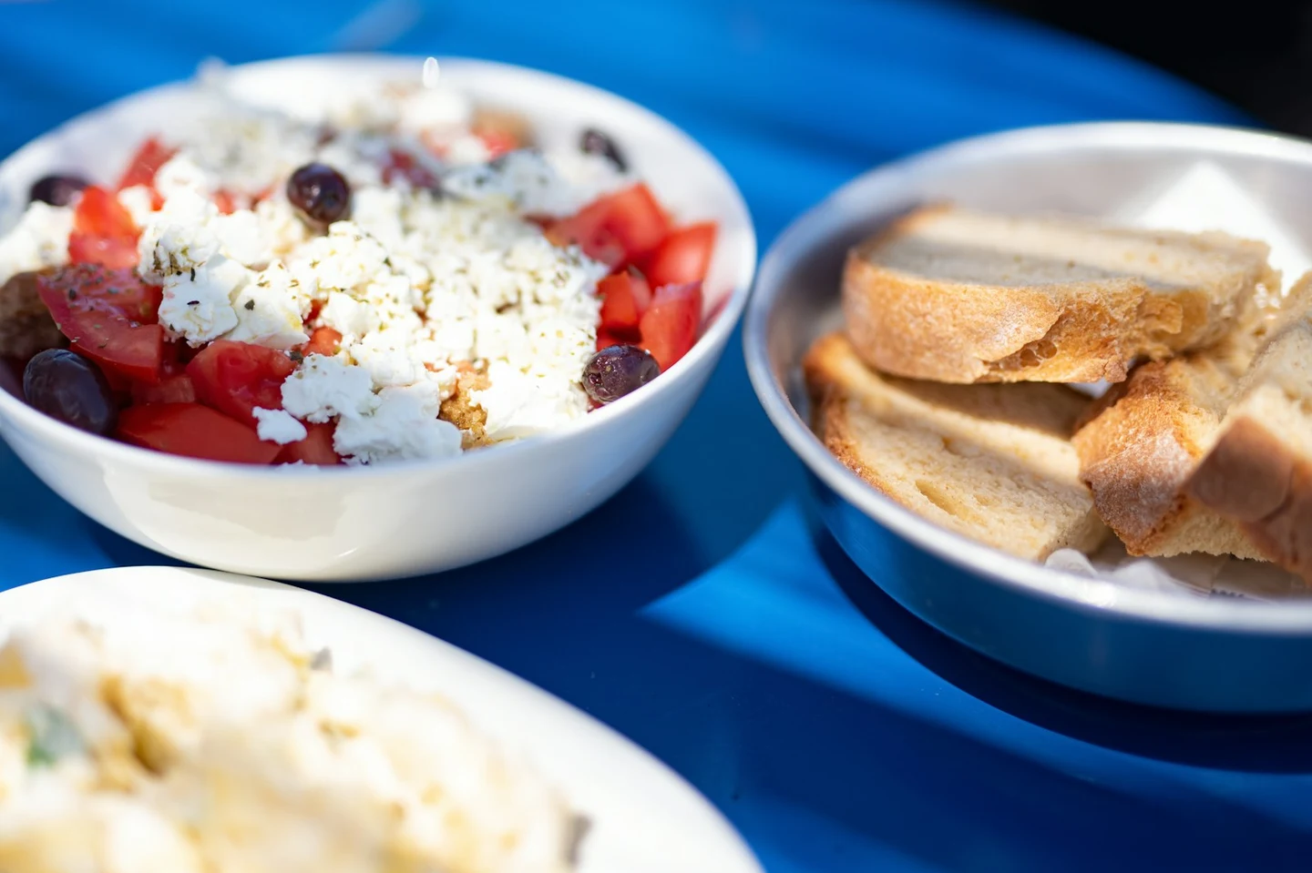 Griechischer Salat mit Feta und Brotkorb auf blauem Tisch