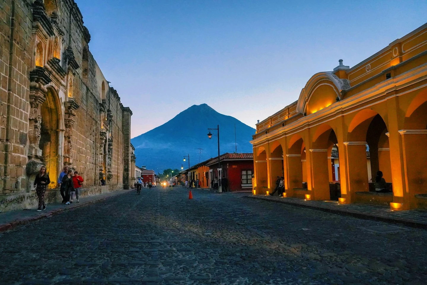 Abendliche Kopfsteinpflasterstraße in Antigua mit beleuchteten Arkaden und Vulkan im Hintergrund