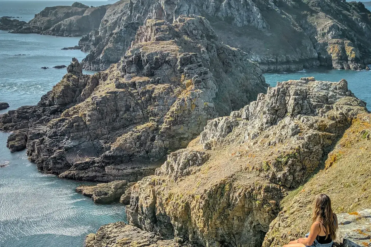 Steile Küste der Insel Sark mit türkisfarbenem Wasser und Wanderin auf den Klippen
