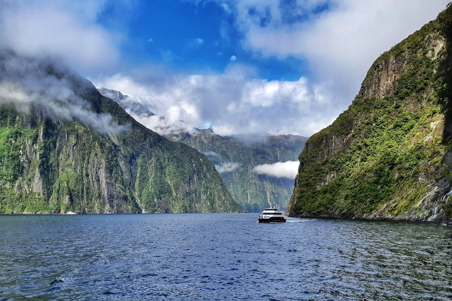 Ausflugsboot im Milford Sound zwischen steilen Fjordwänden