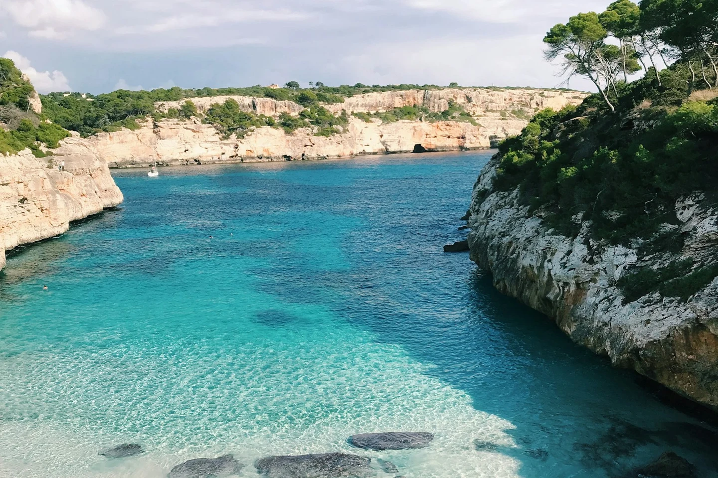 Türkisblaue Badebucht auf Mallorca mit Kalkfelsen und Segelboot