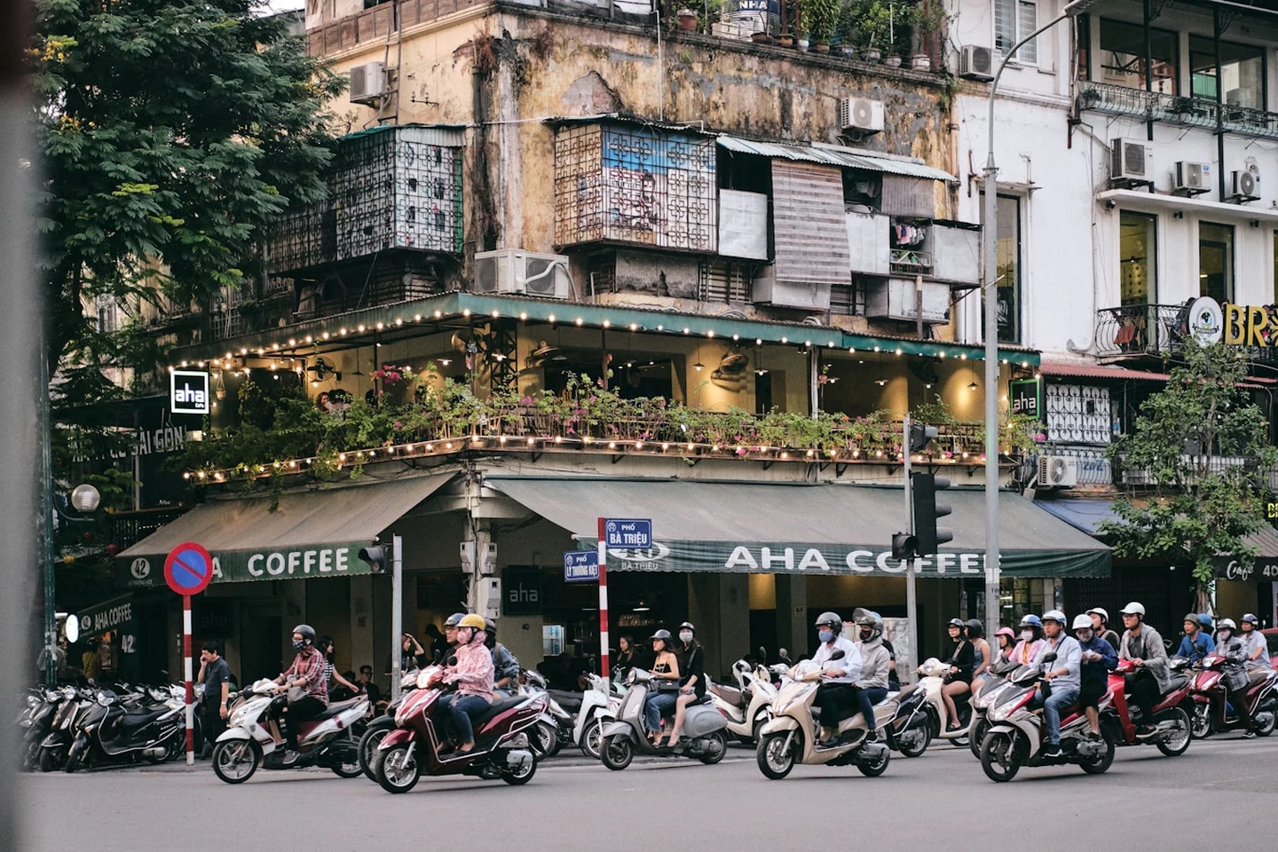 Straßenecke in Hanoi mit Rollerverkehr und Café-Balkon
